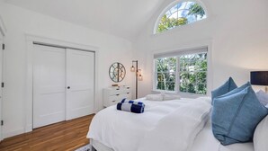 A bedroom with a large bed, a dresser, a mirror, a floor lamp, and a window with a view of trees. - COLONIAL COMPOUND WITH OVERSIZED LIVING ROOMS, GYM, AND ARCADE ROOM, CLOSE... (Southampton)