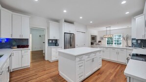 A spacious kitchen with white cabinetry, a central island, and a stainless steel refrigerator. - COLONIAL COMPOUND WITH OVERSIZED LIVING ROOMS, GYM, AND ARCADE ROOM, CLOSE... (Southampton)