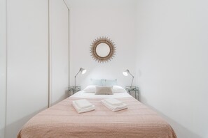 A neatly made bed with a pink blanket, two bedside lamps, and a wall-mounted mirror. - Nomad's Boulevard Flats - Suite & Terrace 1 (Oporto)