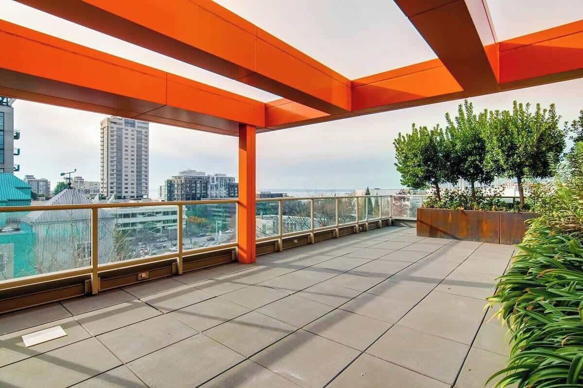 Une vaste terrasse sur le toit offrant une vue dégagée sur les gratte-ciel de la ville, avec des bâtiments modernes et une étendue d’eau visible au loin.