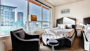 Quarto de hotel moderno com uma janela grande, uma cama, uma cadeira e uma mesa pequena.