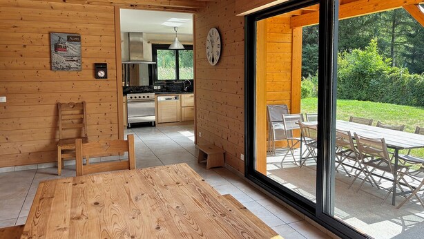 A modern kitchen with wooden walls, a dining area with a large table, and a view of a garden through a sliding door. - BOURG D'OISANS/ALPE d'HUEZ ★ CHALET Bois & Nature with panoramic view (LE BOURG D'OISANS)