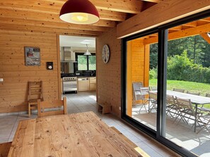 Eine moderne Küche mit Holzwänden, ein Essbereich mit großem Tisch und Blick auf einen Garten durch eine Schiebetür.
