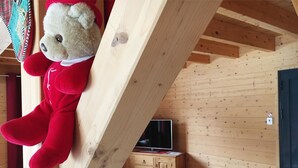 A teddy bear in a red outfit leaning against a wooden beam in a room with a television and a blue door. - BOURG D'OISANS/ALPE d'HUEZ ★ CHALET Bois & Nature with panoramic view (LE BOURG D'OISANS)