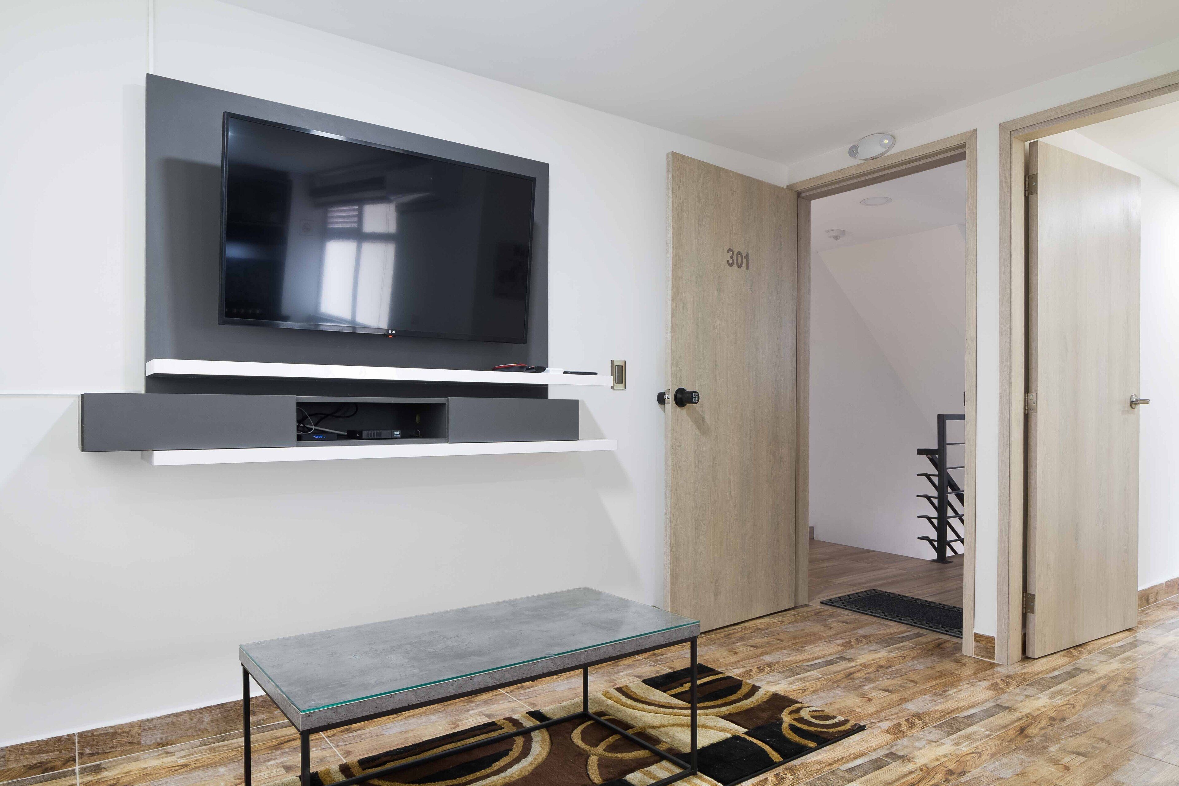 Ein modernes Zimmer mit einem Wand-Fernseher, einem Glastisch und einer Holztür mit der Nummer 301.
