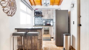 Une cuisine moderne avec un plafond en bois, un réfrigérateur en acier inoxydable, un four à micro-ondes et un évier. On y trouve deux tabourets de bar et une poubelle.
