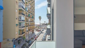 Een balkon met uitzicht op een drukke straat, een grijze bank en een hanglamp.