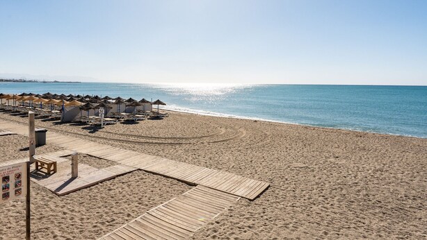 Een strand met houten steegjes, strandparasols en ligstoelen.