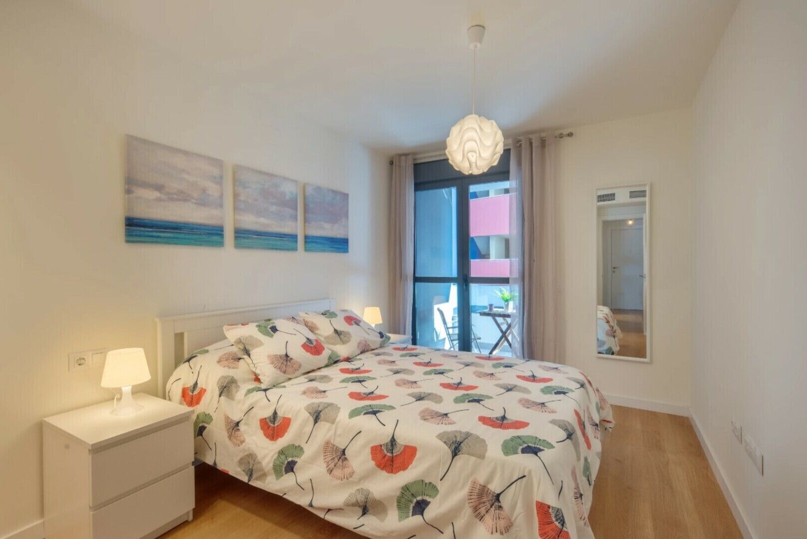Une chambre à coucher avec un lit, une table de chevet, une lampe et une vue sur le balcon extérieur.