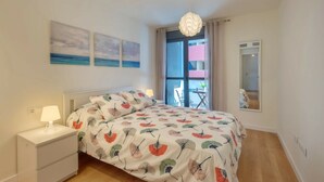 Een slaapkamer met een bed, nachtkastje, lamp en uitzicht op het balkon.