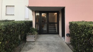 A building entrance with a glass door, a small wooden planter, and a concrete pathway. - PRETTY GROUND FLOOR CONTEMPORARY GARDEN BROWN (Cap d'Agde)