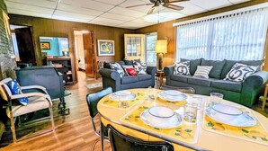 A dining area with a table set for four, a sofa, and a TV in the background. - Sixties Nostalgia - Rhele's Roost at Silver Lake Dunes (Mears)