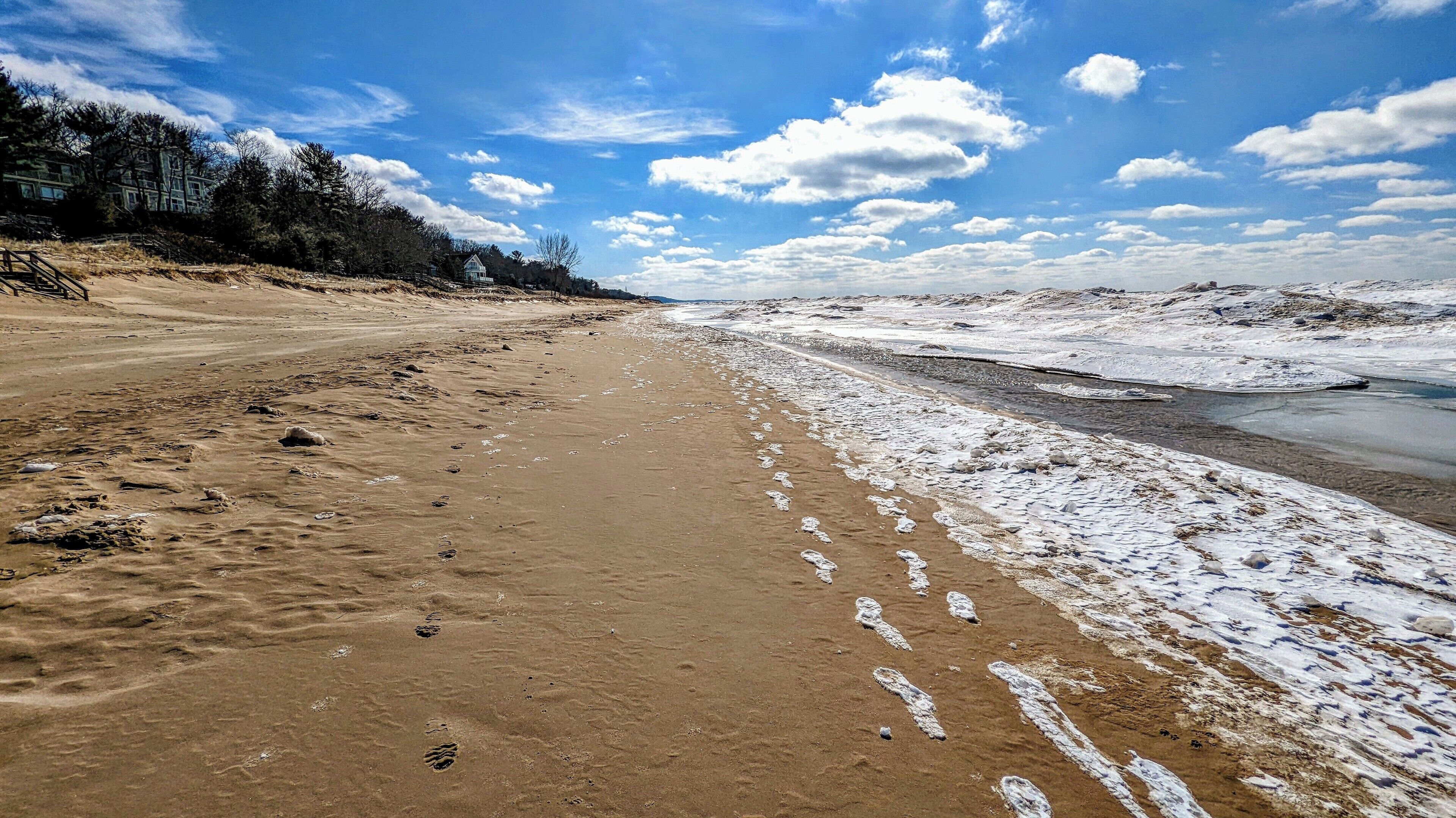 A sandy beach with footprints leading to a snow-covered area.
