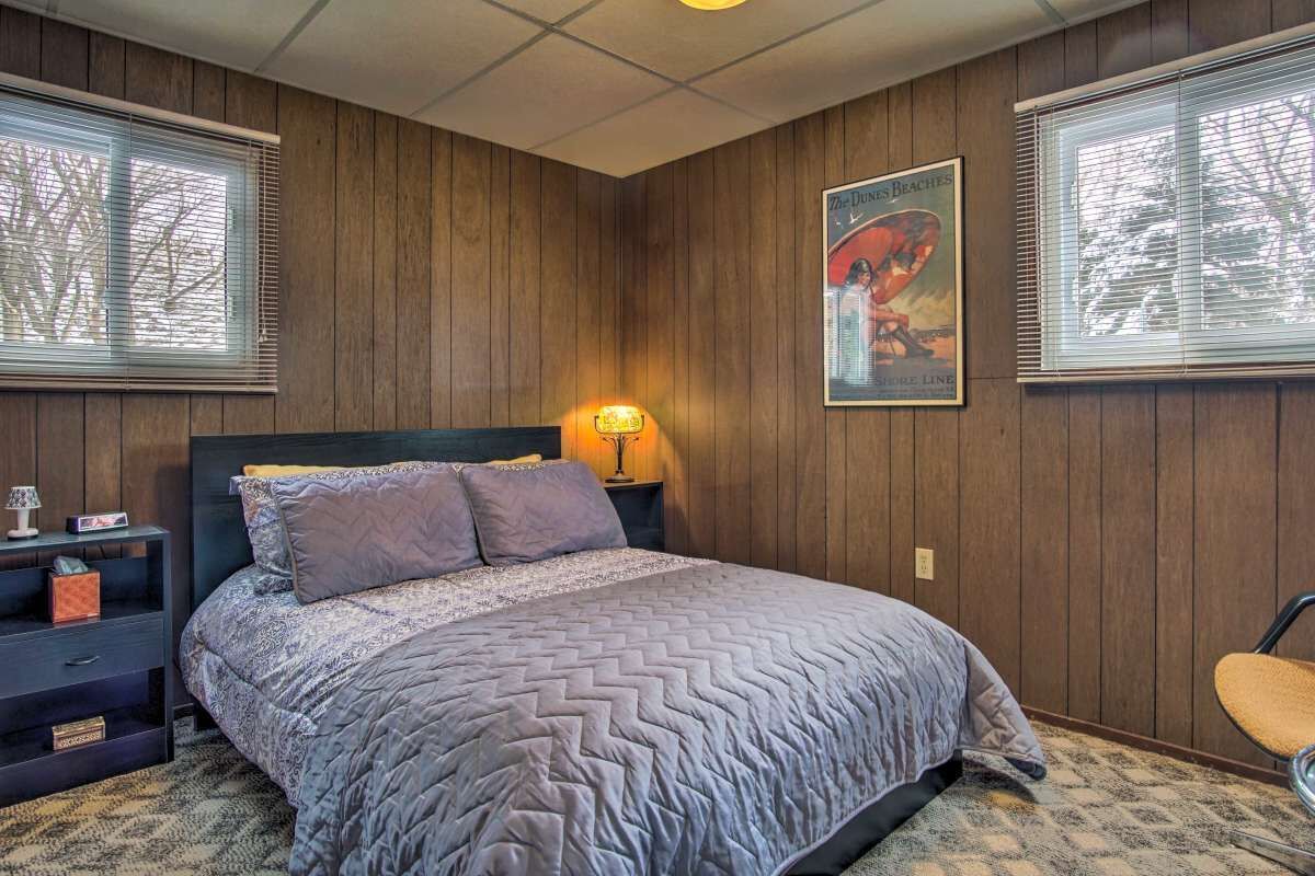 Un dormitorio con pared de paneles de madera, una cama con colcha estampada, una mesita de noche con lámpara y un cuadro en la pared.