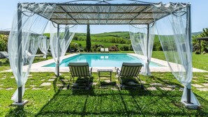 Uma área externa coberta com piscina, duas cadeiras e uma mesa.