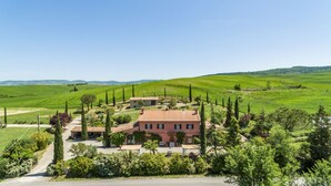 Uma casa grande cercada por campos verdes exuberantes e altas árvores de cipreste.