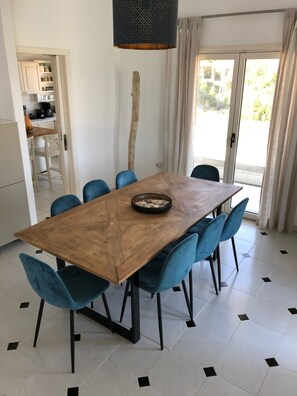 Spiseområde med et træbord og blå stole, en hængende lysarmatur samt udsigt til det frie gennem en glasdør.