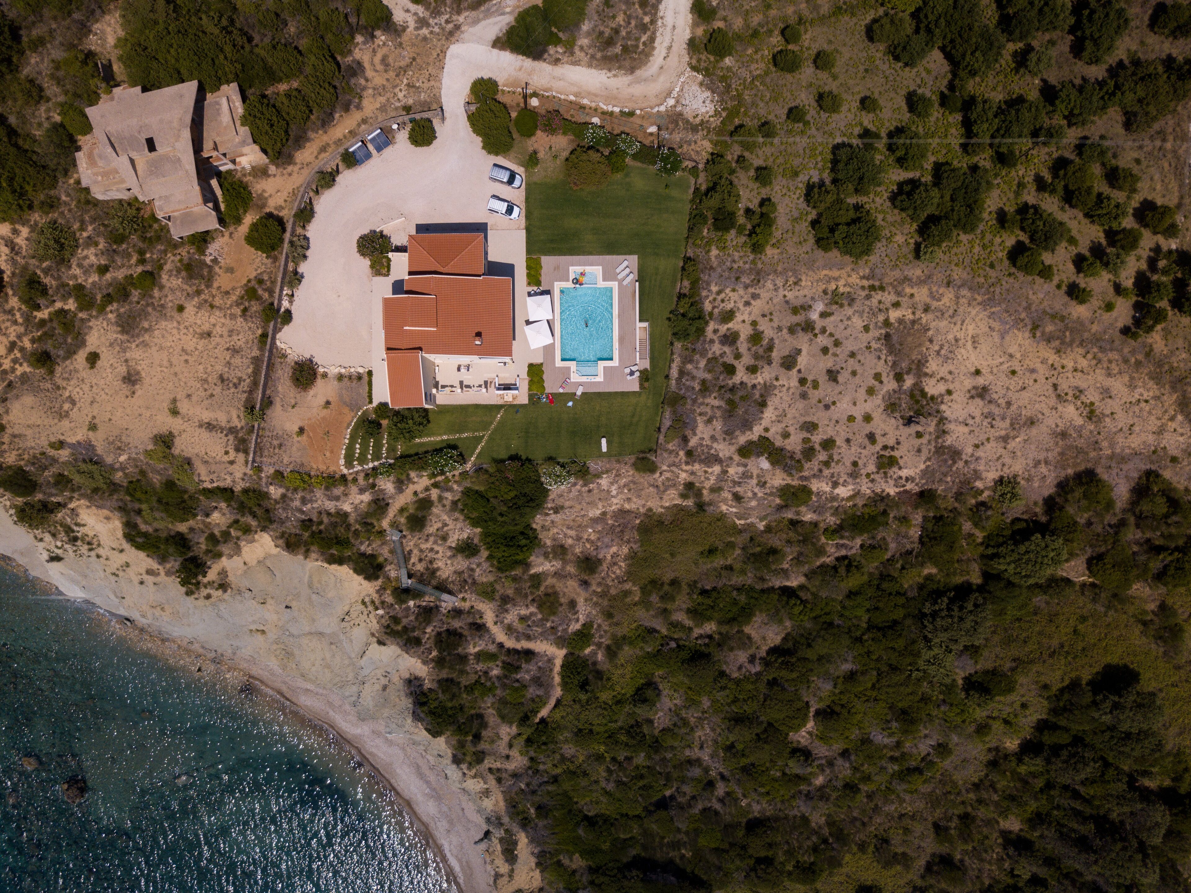 Luchtbeeld van een landgoed aan de kust met een zwembad, een groot huis en een strand.