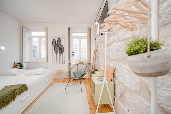 A modern bedroom with a bed, a chair, a hanging plant, and artwork on the wall.