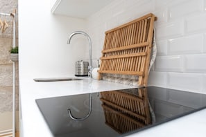 A modern kitchen with a stainless steel sink, a wooden rack, and a white tiled backsplash.