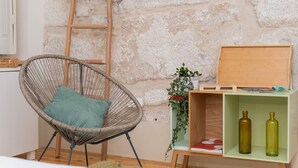 Une chaise en osier avec un coussin, une échelle en bois et une étagère verte sur laquelle se trouvent deux bouteilles et une plante.