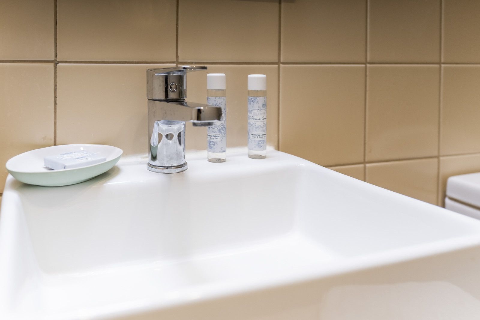 Un lavamanos blanco con grifo de cromo, un jabonera y dos botellas de productos de baño.