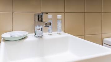 Un lavamanos blanco con grifo de cromo, un jabonera y dos botellas de productos de baño.