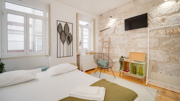 Une chambre avec un lit, une chaise, un téléviseur et un mur en pierre.