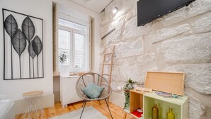 Un salon moderne avec un mur en pierre, un fauteuil en osier, un meuble en bois contenant des bouteilles et une grande fenêtre.