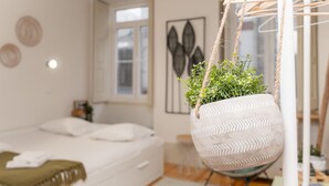 Une chambre à coucher avec un lit, une plante suspendue, une fenêtre et une porte.