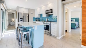 Una cocina moderna con una isla central, electrodomésticos de acero inoxidable y salpicadero de azulejos azules.