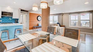 Una cocina moderna con microondas, estufa y azulejos azules. Hay un comedor con una mesa de vidrio, sillas y un pilar decorativo tejido.