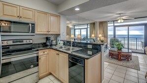 A modern kitchen with built-in appliances, a dining area with a view of the ocean, and a balcony with a ceiling fan. - 🌊🌞Lazy River + Indoor/Outdoor Pools | Oceanfront | South Wind 504 (Myrtle Beach)