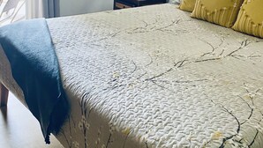 Un dormitorio con cama, mesita de noche, lámpara, cuadro enmarco y ventana con cortinas.