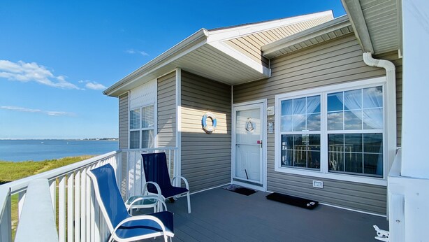 A deck with two chairs and a lifebuoy on a house by the water.