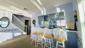 A kitchen with a bar area, white bar stools, a large mirror, and a staircase leading to another level.