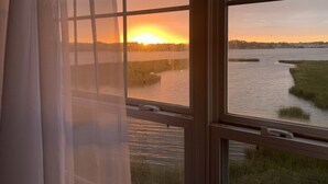 A view through a window with a curtain, overlooking a body of water and a sunset.