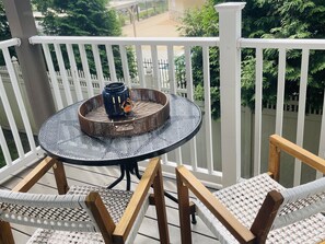 Een ronde tafel met een geweven decoratiestuk, omringd door rieten stoelen op een balkon met witte relingen.
