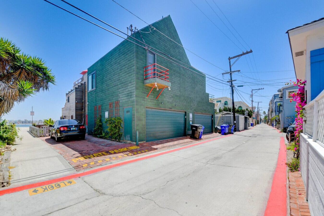 A narrow street with a green building, a parked car, and a red curb.