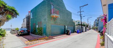A narrow street with a green building, a parked car, and a red curb.