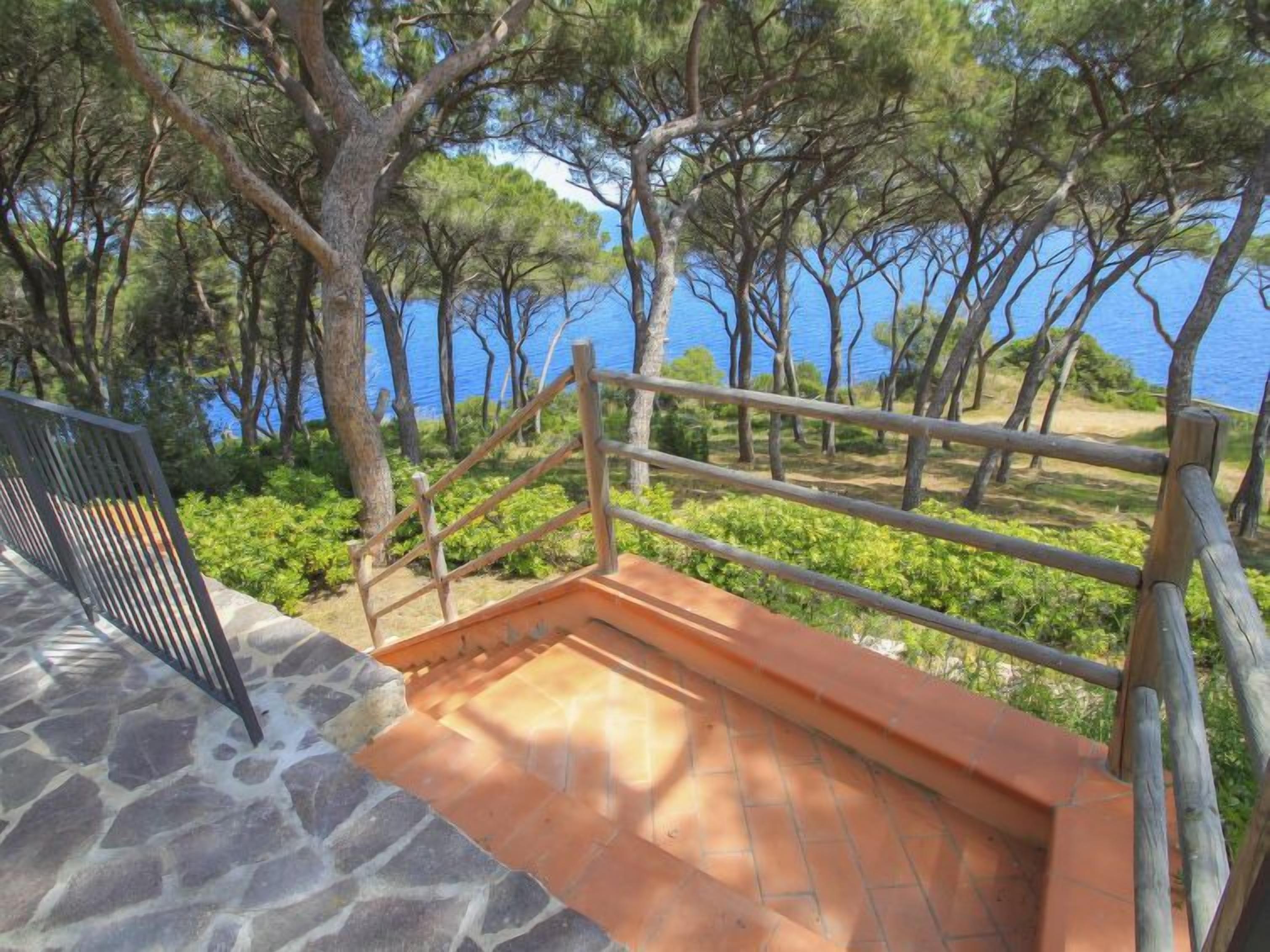 A stone staircase leading to a wooden deck with a metal railing overlooking a body of water and trees.