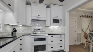 Una cocina con armarios blancos, encimera negra y alfombra estampada.
