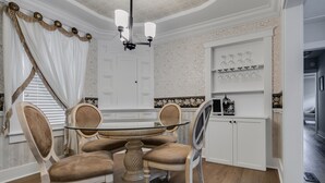 Comedor con mesa de vidrio rodeada de sillas tapizadas, candelabro y un aparador blanco con cristalería.
