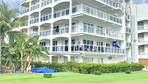 A multi-story hotel with balconies, a well-maintained lawn, and palm trees. - Maho Beach House: Sunset Suite, 1-Bedroom (Maho)