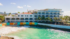 Et hotel med flere etager, altaner, en strand foran og palmer.