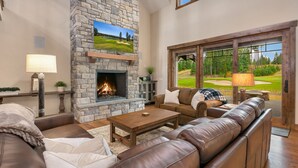 Una sala de estar acogedora con chimenea de piedra, sofás de cuero y una televisión grande mostrando un campo de golf.