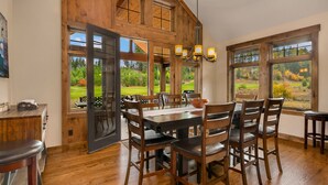 Un comedor con una gran mesa de madera, varias sillas y vistas a un jardín a través de amplios ventanales.