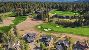 Un campo de golf con varios edificios, rodeado de densos bosques y montañas.
