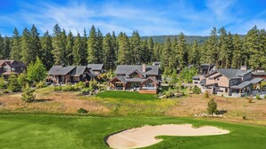 Un campo de golf con un búnker de arena y un conjunto de casas modernas con amplias ventanas y un patio cubierto.