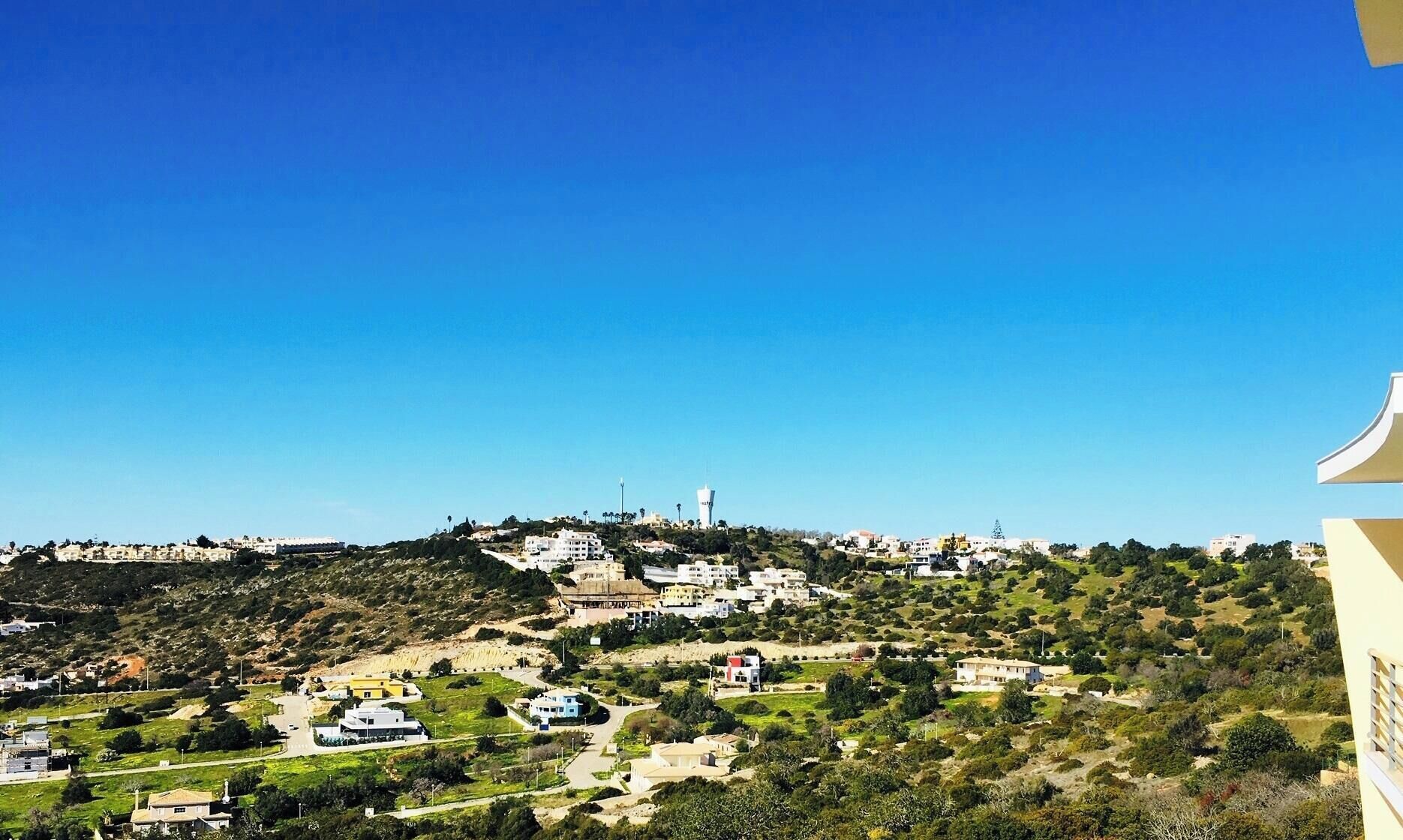 A panoramic view of a hilly town with buildings and greenery.